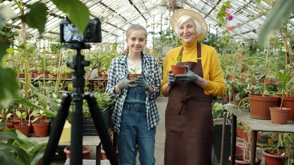 Grandmother and Granddaughter Vloggers Recording Video in Greenhouse Showing Thumbsup Gesture