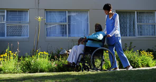Side view of Caucasian female doctor pushing senior patient in wheelchair at nursing home 4k