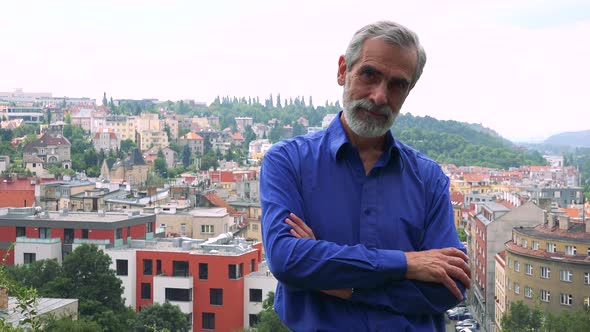 Old Senior Man Looks To Camera with Self-confident Face - City (Buildings) in Background