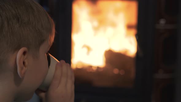 Little Kid Boy Sit by Burning Fireplace Watch Fire, and Enjoy a Hot Tee Cozy Atmosphere