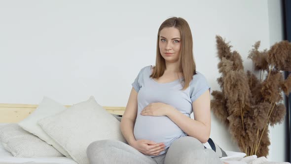 Pregnant Woman in Home Clothes Sitting on a Double Bed