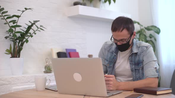 Young Caucasian Man Stay Home Working From Home Wearing Protective Mask Using Laptop and Internet