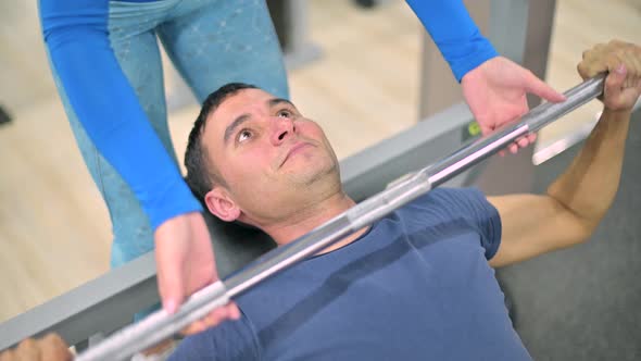 skinny guy does bench press under the supervision of a trainer