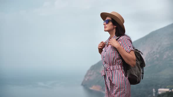 Trendy Female Hiker with Backpack Relaxing on Top of High Mountain Over Sea Enjoying Freedom