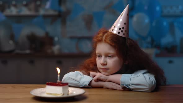 Upset Little Girl with Long Red Curly Hair Sitting at Table with Head Down on Hands