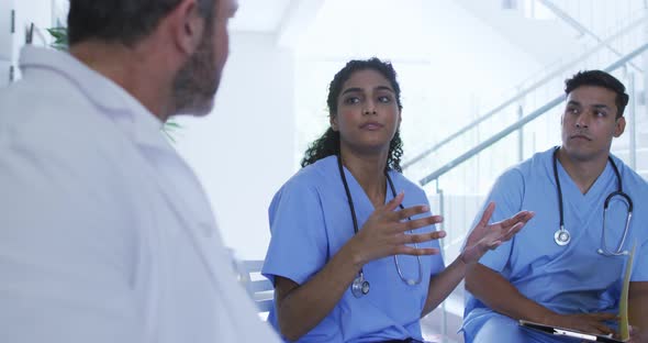 Asian female doctor sitting and discussing with diverse male colleagues at hospital staff meeting