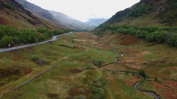 Cinematic drone shot of scottish highland valley with car passing by on windind road in background