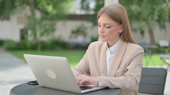 Young Businesswoman with Laptop Smiling at Camera in Outdoor Cafe