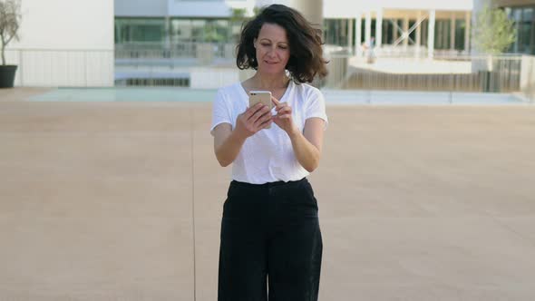 Beautiful Smiling Woman Walking with Smartphone on Street