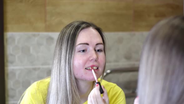 Young woman with fair hair is applying pink lipstick