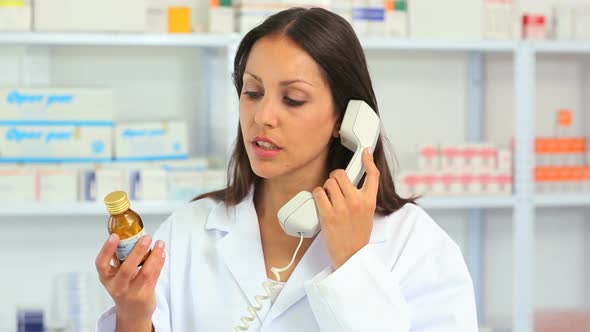 Female pharmacist calling while holding a bottle of drug