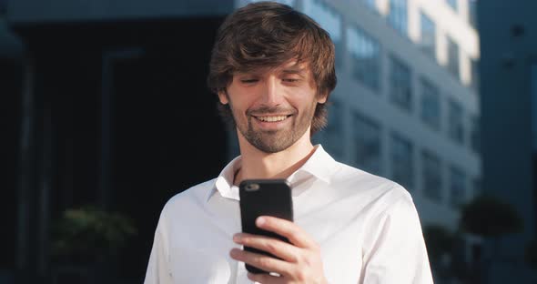 Closeup of Handsome Young Businessman using his Smartphone and Smiles.