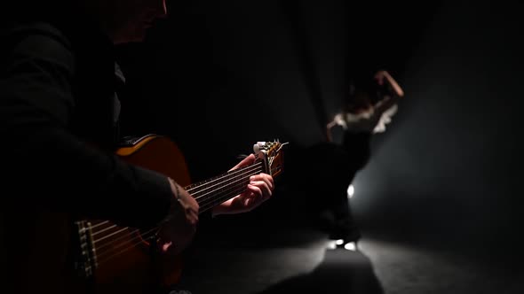 Man on the Guitar Plays a Flamenco Girl Dancing. Light From Behind. Smoke Black Background