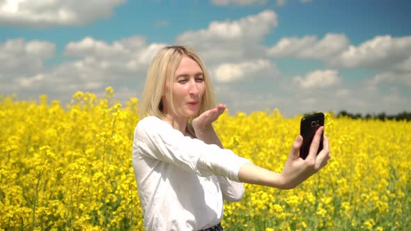 Portrait of a Happy Woman Taking Selfie in a Field of Yellow Rapeseed Flowers