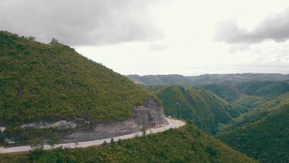 Aerial drone footage flying towards a mountain with a road carved into the side in central Cebu near