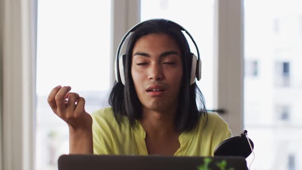 Mixed race gender fluid person recording a podcast using laptop at home