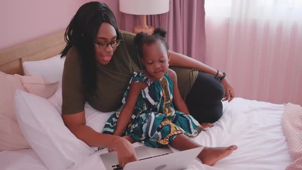 African American mother use laptop with her daughter on bed during day time