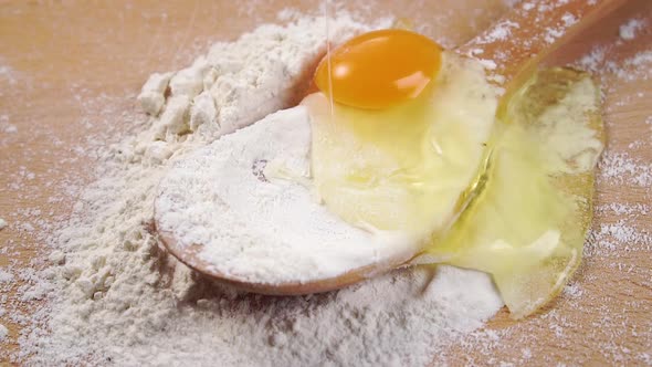 Raw egg falls into a pile of white flour in a wooden spoon