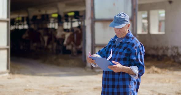 Farmer Gesturing While Writing on Clipboard Against Barn