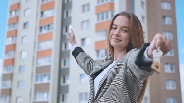 The Girl Shows the Keys to the Apartment Against the Backdrop of an Apartment Building