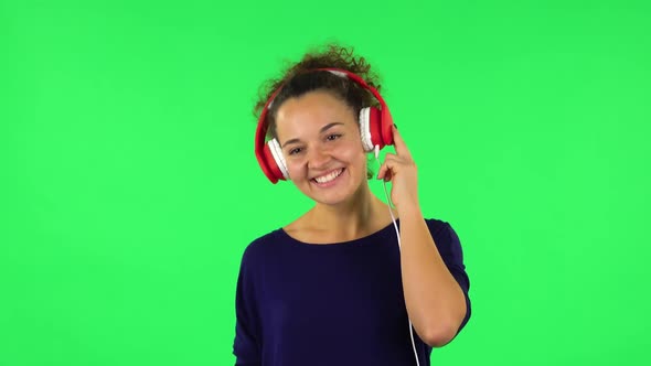 Portrait of Curly Woman Dancing and Enjoying Music in Big Red Headphones. Green Screen