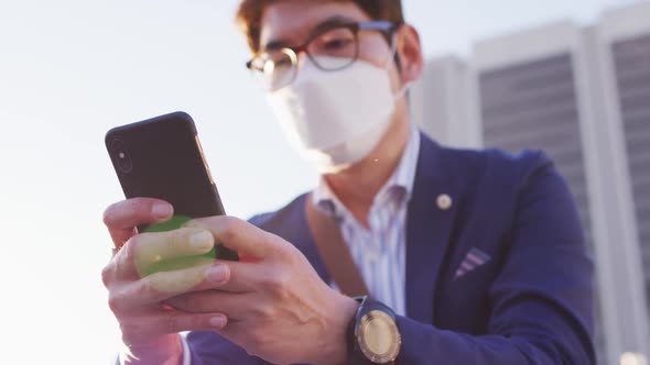 Asian man wearing face mask using smartphone while sitting on the stairs at corporate park