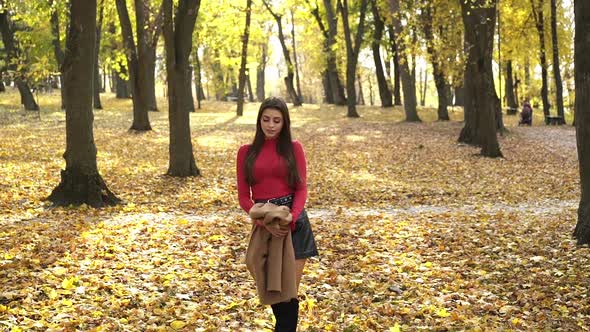 Glamorous Young Girl Walks Enchanted in the Autumn Park and Puts on a Coat