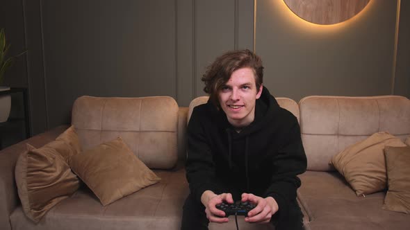 Funny Excited Young Caucasian Man Gamer Holding Joystick Controller Playing Video Games Sitting on