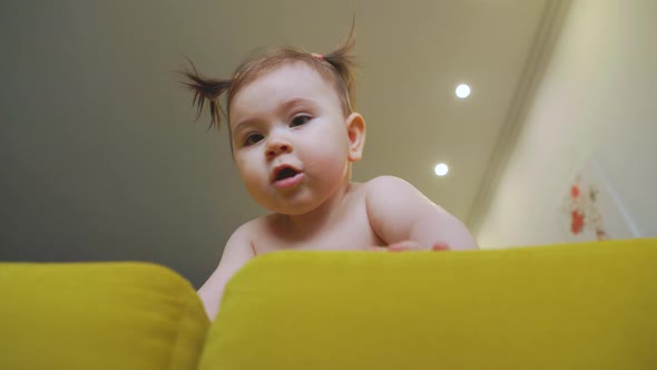 Cute Little Baby Girl on the Yellow Sofa Making First Steps At Home