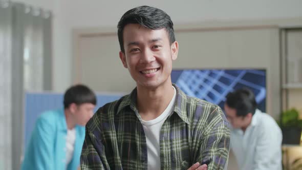 Smiling Asian Man Engineer Crossing His Arms To Camera While His Colleagues Are Discussing Work