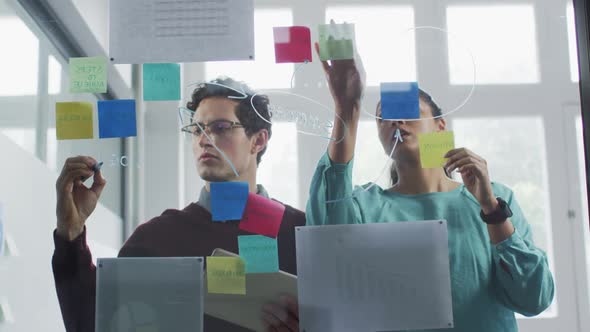 Man and woman discussing over memo notes on glass board at office