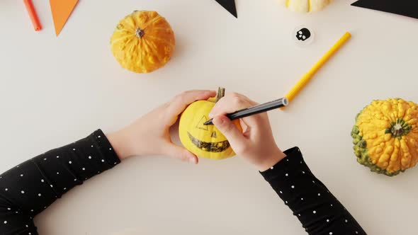 Kid preparing for holiday Halloween. Flat lay hands of children drawing scary face on pumpkin