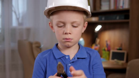 Portrait of a Small Surprised Boy in a Helmet with Tools in His Hands at Home