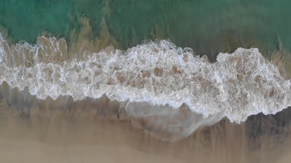 People walk on Matadouro beach with ocean waves crashing on shoreline. Aerial top-down rising