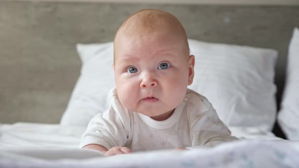 Little Baby Girl Lies on Belly on Parent Bed and Smiles