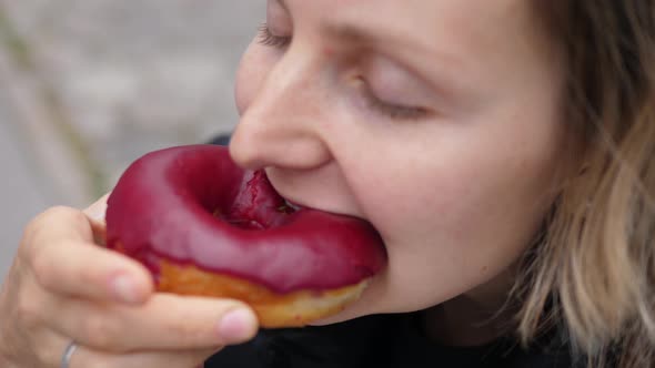 Close Up of a Hungry Woman Taking a Bite of Berry Vegan Doughnut with Her Eyes Closed