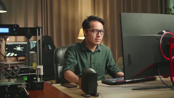 Asian Man Works On Personal Computer And 3D Printer In Home Office, He Works At Night