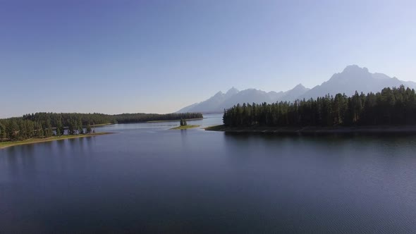 Camera ascends diagonally above a calm Jackson Lake with revealing more water and forest along the h