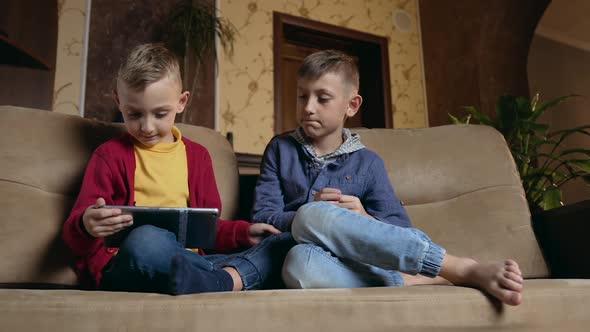 Boys Sitting on Soft Couch at Home and Watching Apps on Tablet Computer or Playing Online Games