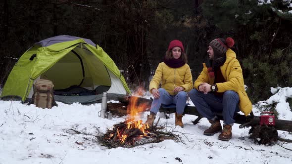 Young Man and Woman Near a Campfire in the Forest in Winter