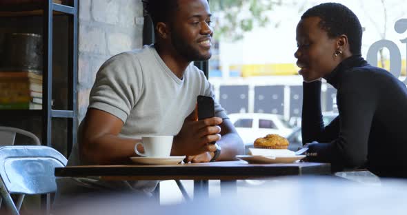 Couple interacting with each other while using mobile phone in cafe 4k