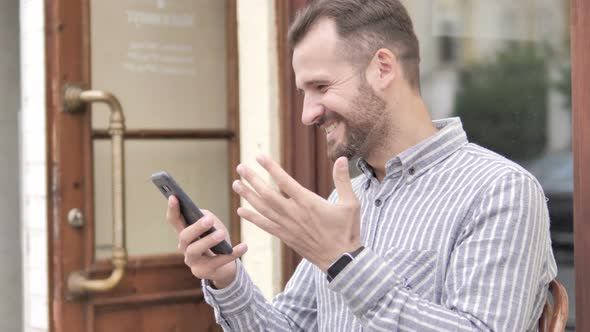 Man Celebrating on Smartphone while Sitting Outdoor