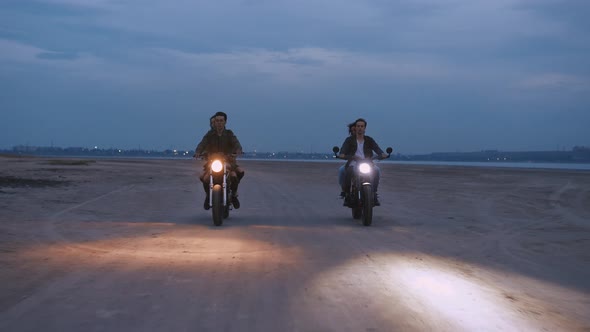Cinematic Shot of Two Young Couples Riding on Vintage Motorcycles After Sunset on Beach Slow Motion