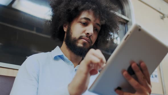 Close-Up Portrait of Young Stylish Hispanic Man Using Cellular Mobile Device in Subway. Curly Man