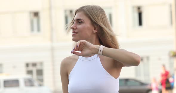 Stylish girl standing, smiling and tuning in her wristwatch.