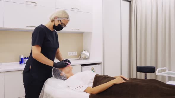 Cosmetologist, in Mask and Gloves, Removes Remains of Cosmetic Face Product, From Female Face with