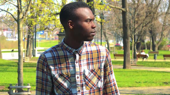 A Young Black Man Covers His Eyes with His Hands, Stops and Looks Around in Confusion in a Park