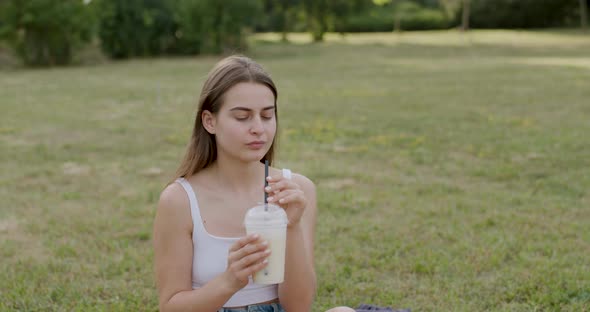 Young Brunette Dressed in White Drinks a White Lemonade and Looks Straight Ahead