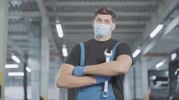 Confident Auto Mechanic in Uniform Working Gloves and Covid19 Face Mask Posing in Repair Shop