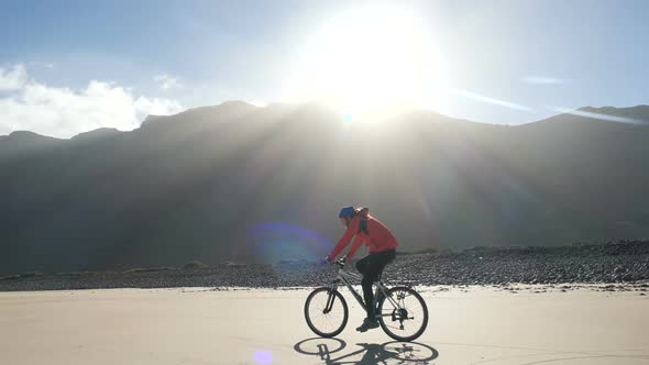 Young Man Rides a Bicycle on a Sand Beach on Canary Islands in Beautiful Sunrise Light Against